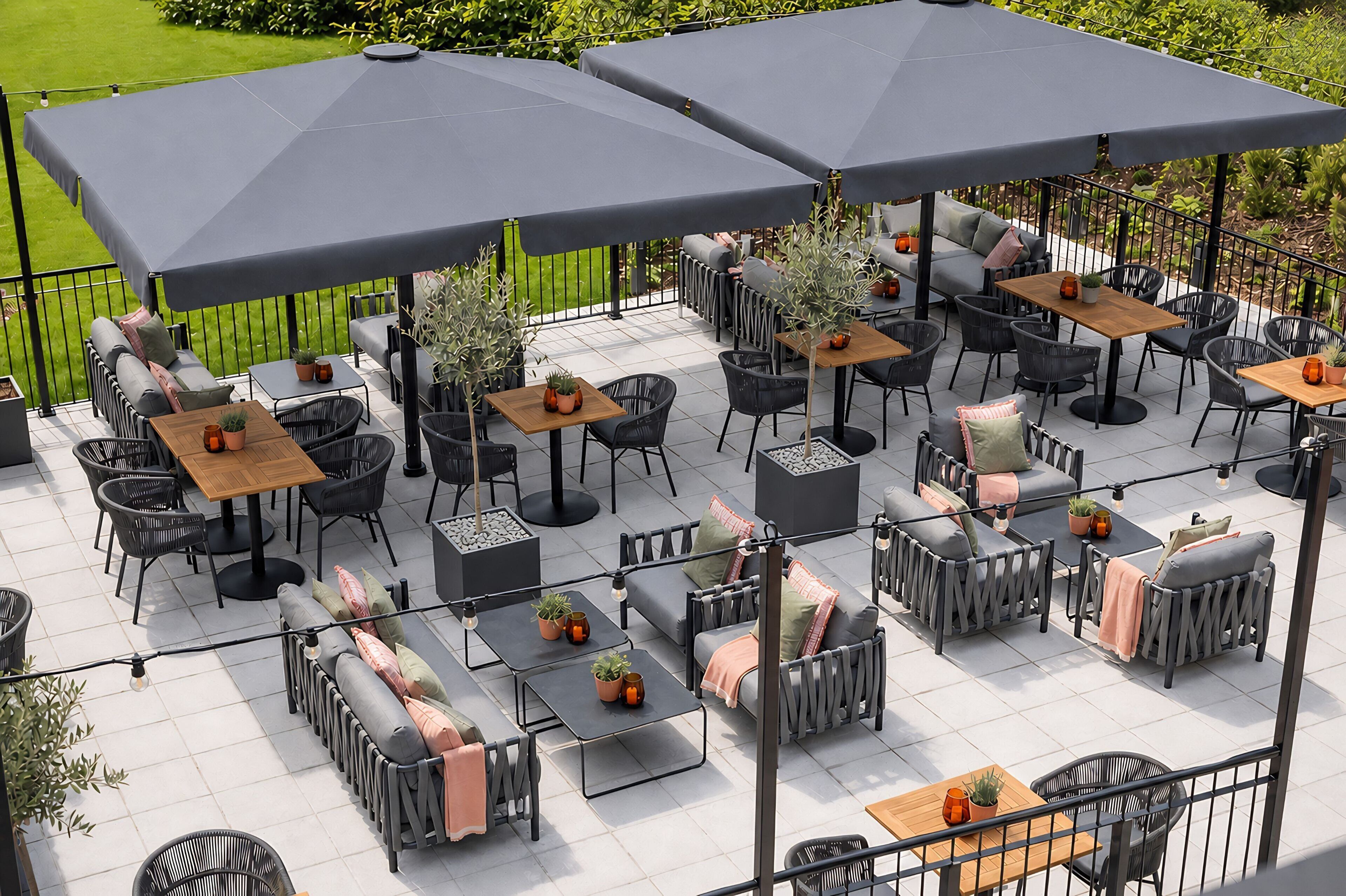 An outdoor patio with multiple tables and chairs, some with umbrellas, surrounded by greenery.
