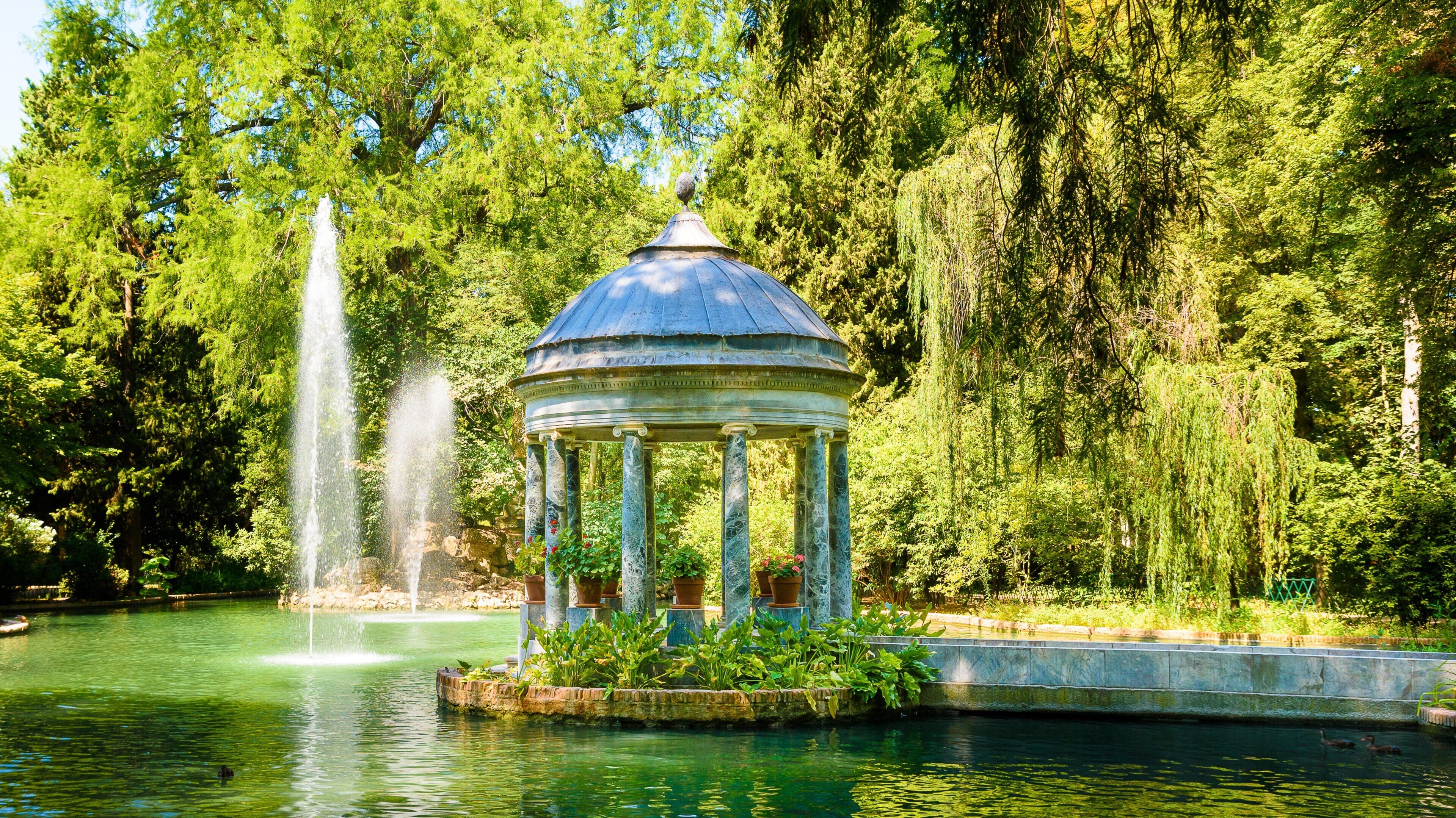 A gazebo with a fountain in a lush garden.