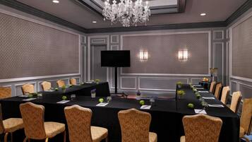 A conference room with a long table, chairs, a chandelier, and a flat-screen TV.