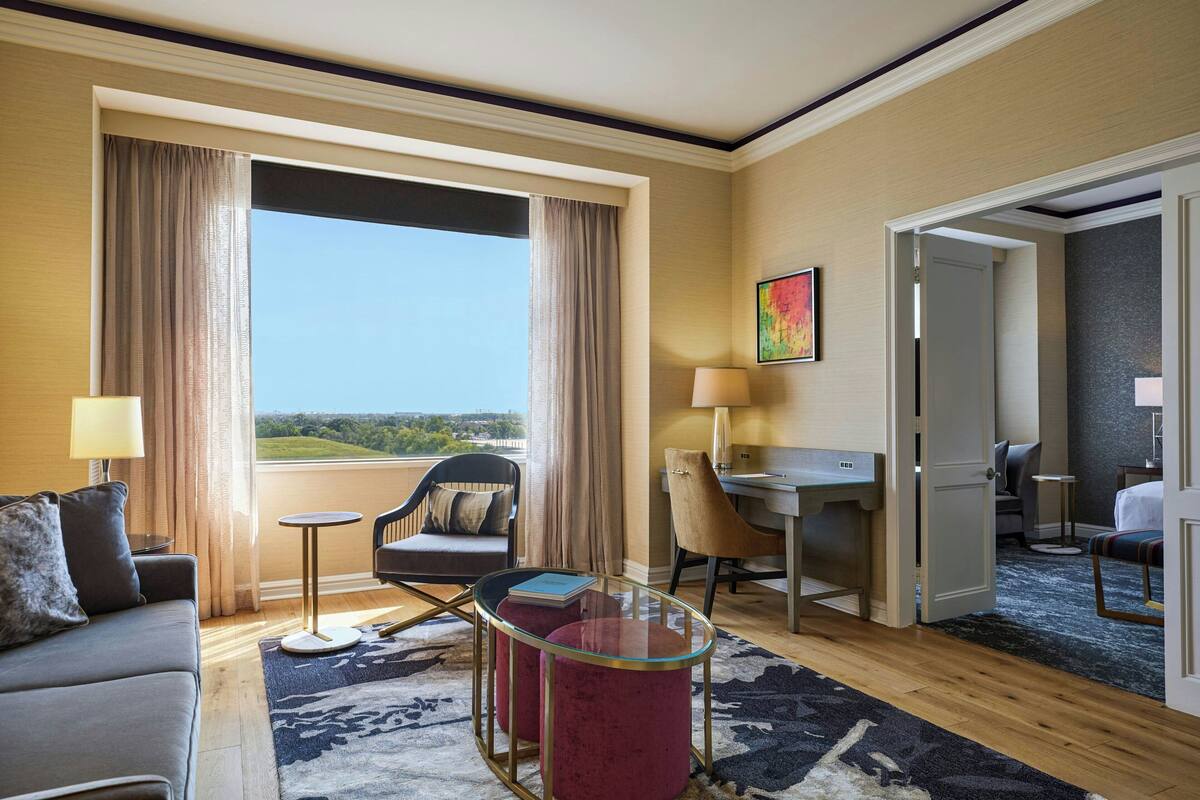 A hotel room with a large window, a sofa, a desk, a chair, and a small table.
