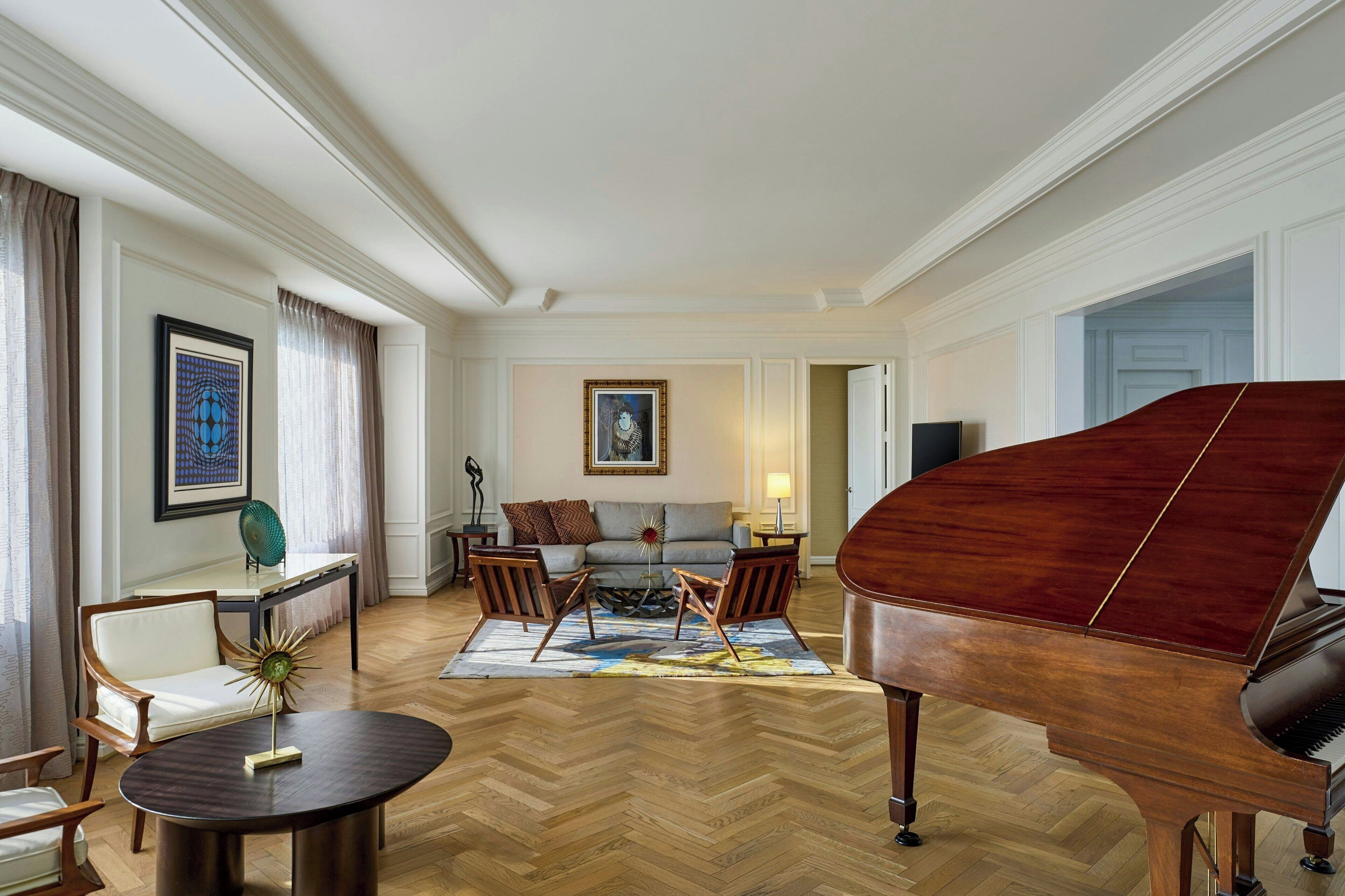 A spacious living room with a grand piano, a sofa set, and a herringbone wood floor.