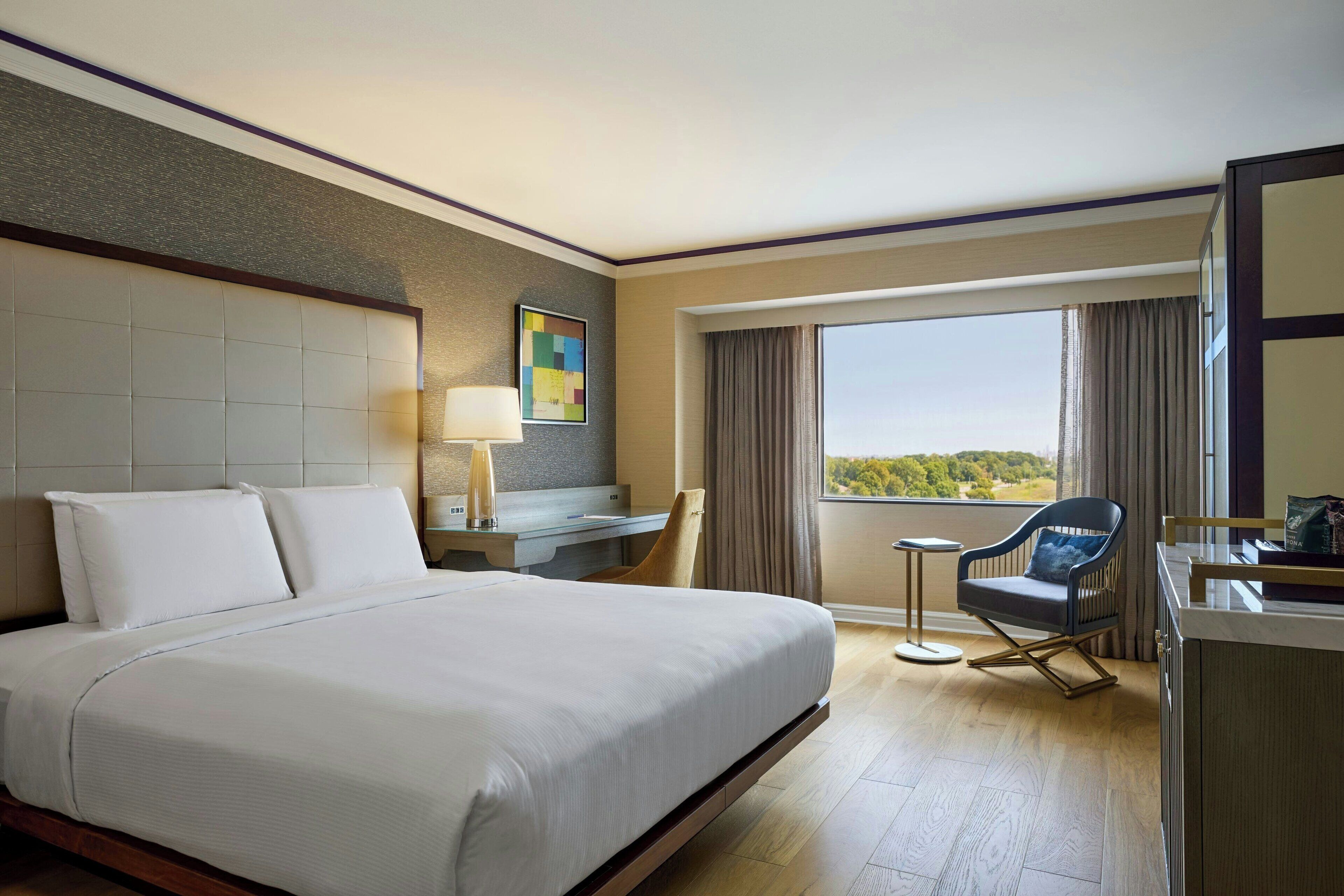 Une chambre d’hôtel avec un grand lit, un bureau avec une lampe, une chaise, une petite table et une vue sur l’extérieur.