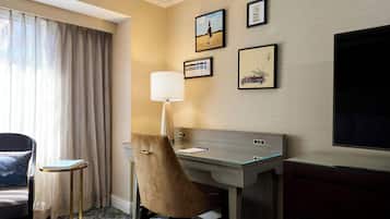 Una habitación de hotel con escritorio, silla, lámpara y una obra de arte en la pared.