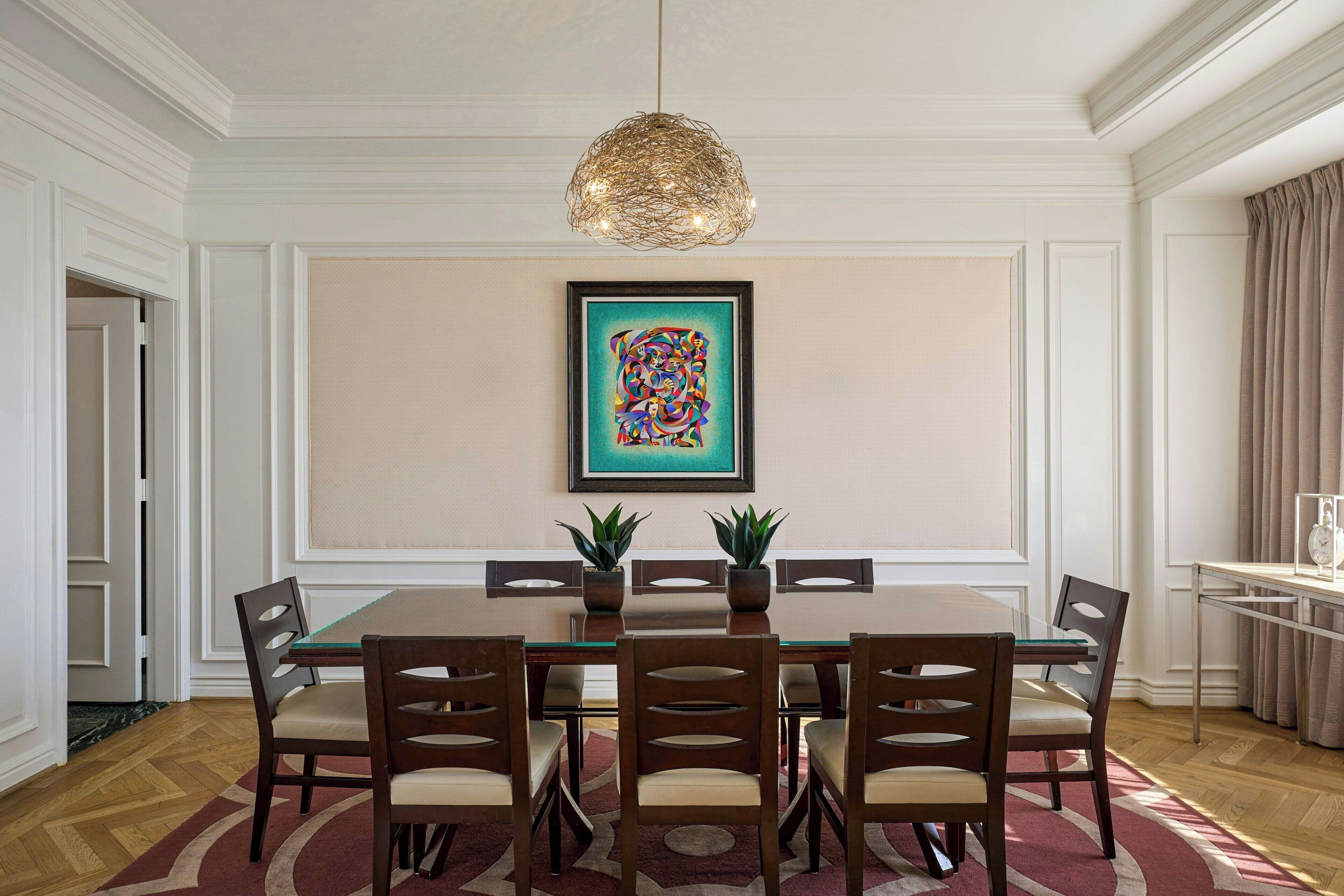 Ein Esszimmer mit einem rechteckigen Tisch, sechs Stühlen, zwei Topfpflanzen, einem gerahmten Kunstwerk an der Wand und einer Pendelleuchte.