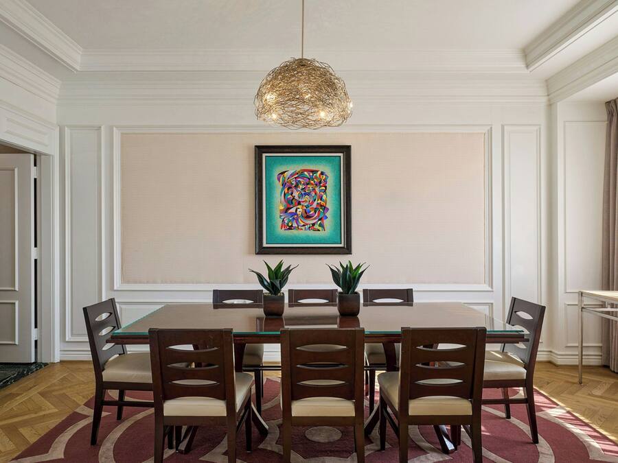 Ein Esszimmer mit einem rechteckigen Tisch, sechs Stühlen, zwei Topfpflanzen, einem gerahmten Kunstwerk an der Wand und einer Pendelleuchte.