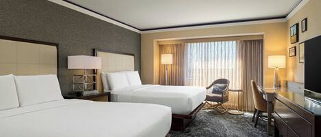 Quarto de hotel com duas camas, uma escrivaninha, uma cadeira, uma televisão e uma janela com cortinas.