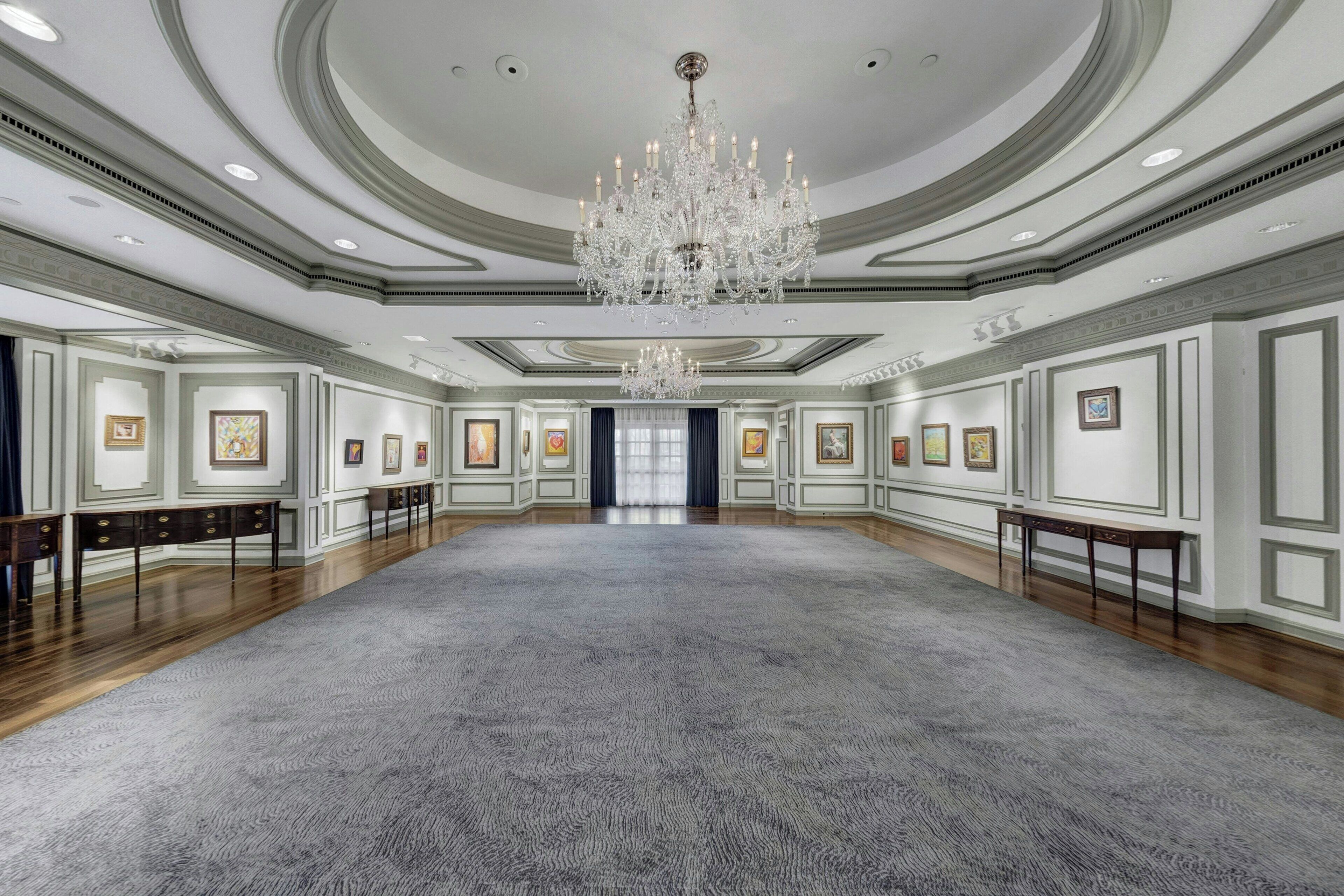 A spacious room with a large chandelier, framed artwork on the walls, and a patterned carpet.