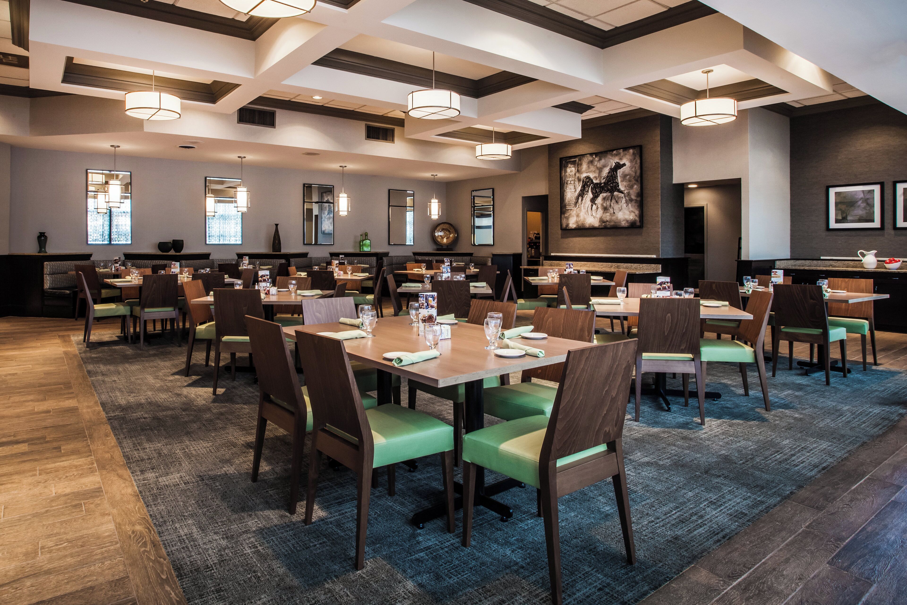 A spacious restaurant with multiple dining tables and chairs, large windows, and modern lighting fixtures.