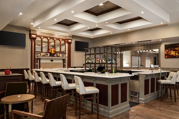 Uma área de bar moderna com uma ilha central, banquetas e um espelho grande acima do balcão.