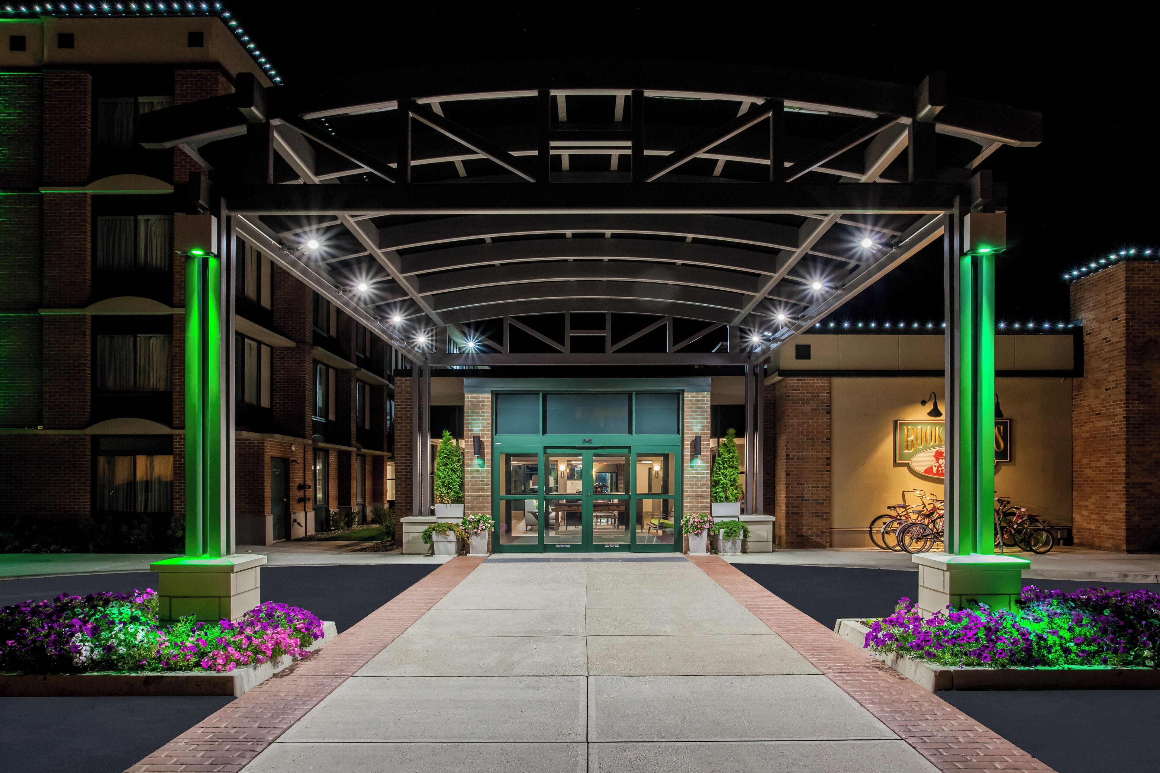 A hotel entrance with a covered walkway, a green-lit entrance, and a bike parking area.