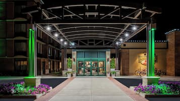 A hotel entrance with a covered walkway, a green-lit entrance, and a bike parking area.