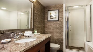A bathroom with a marble sink, a large mirror, a framed picture on the wall, a toilet, and a glass-enclosed shower.