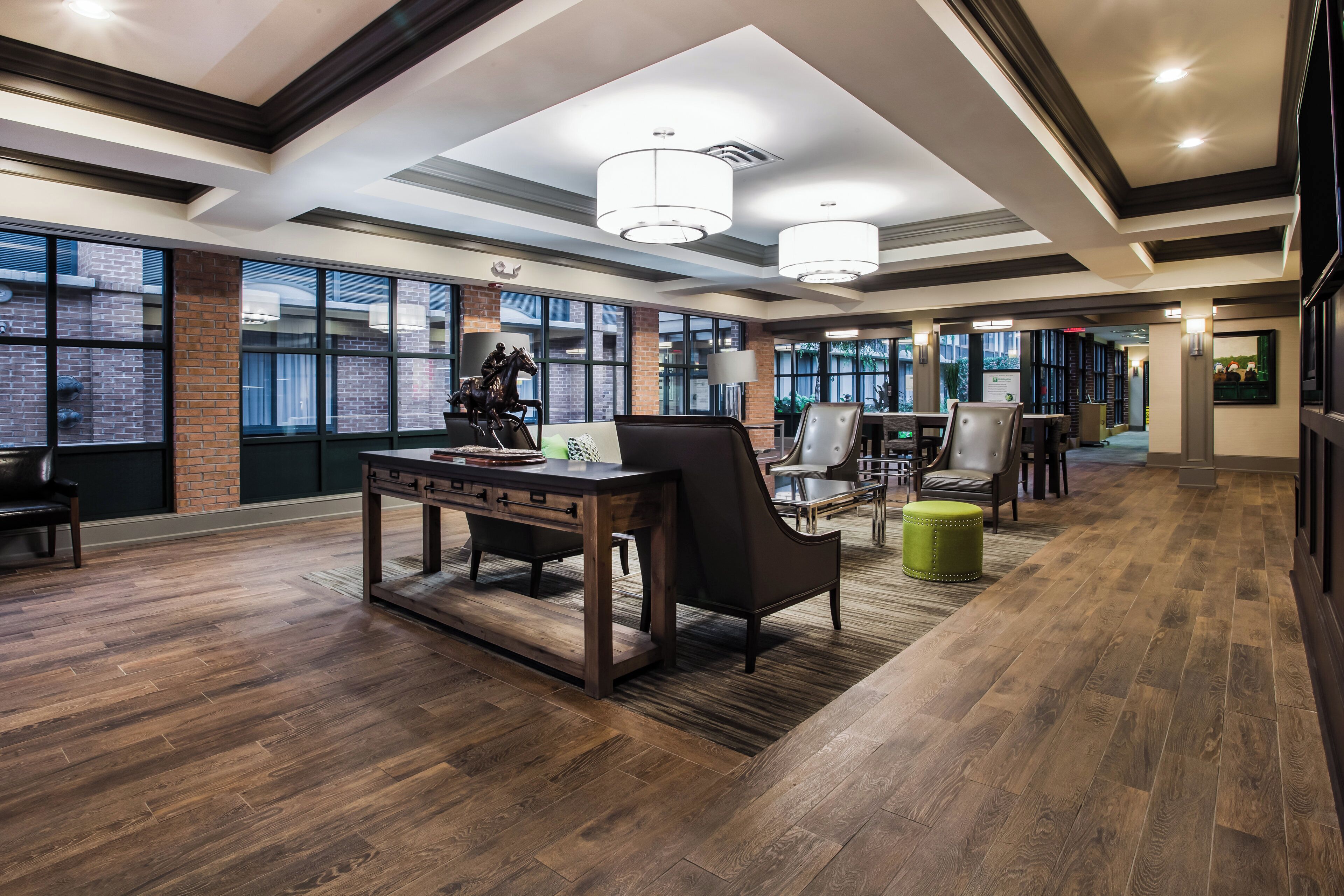Eine großzügige Hotelhalle mit einem großen Schreibtisch, Ledersesseln und einem grünen Hocker.