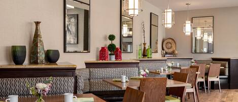 A restaurant with wooden tables and chairs, a patterned bench, and hanging pendant lights.
