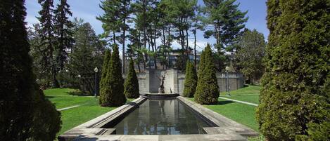Un jardín formal con fuente central, setos recortados y altos árboles.