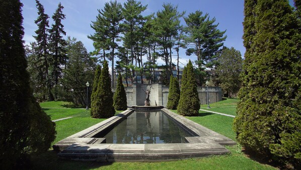 A formal garden with a central water feature, trimmed hedges, and tall trees. - Holiday Inn Saratoga Springs by IHG (Saratoga Springs)