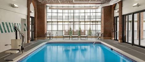 An indoor swimming pool with clear blue water, surrounded by brick walls and large windows.