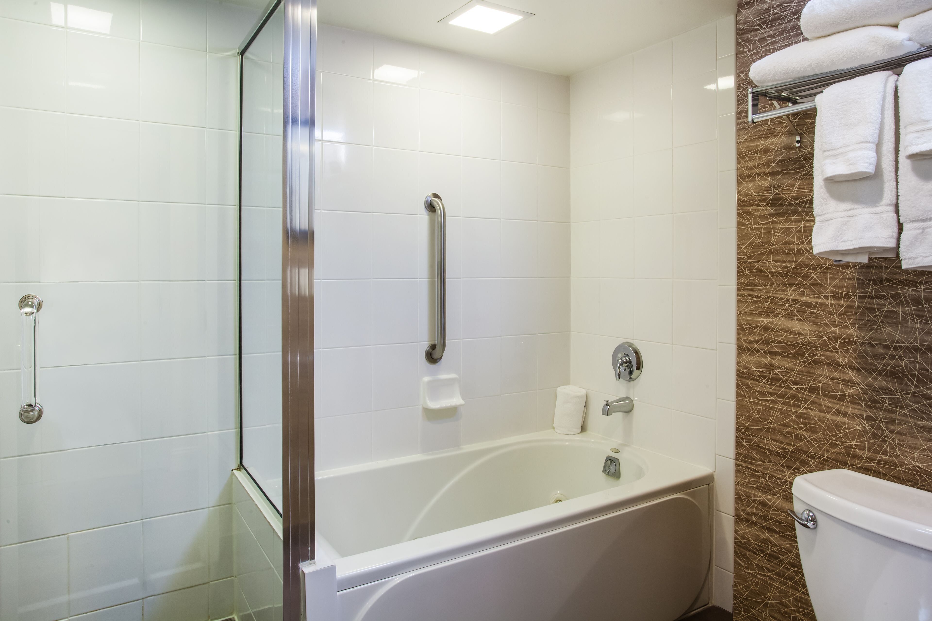 Un baño con bañera, cabina de ducha de vidrio, inodoro y toallero.