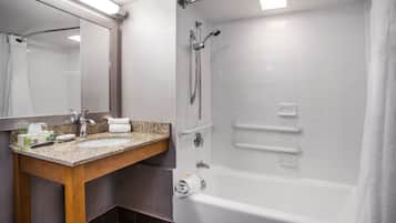 A modern bathroom with a granite countertop sink, a large mirror, a bathtub, and a shower with grab bars.
