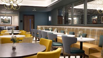 Un restaurante con mesas redondas y sillas amarillas, un área con bancos para sentarse y un candelabro.