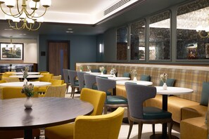 Un restaurant avec des tables rondes et des chaises jaunes, un espace avec des banquettes et un lustre.