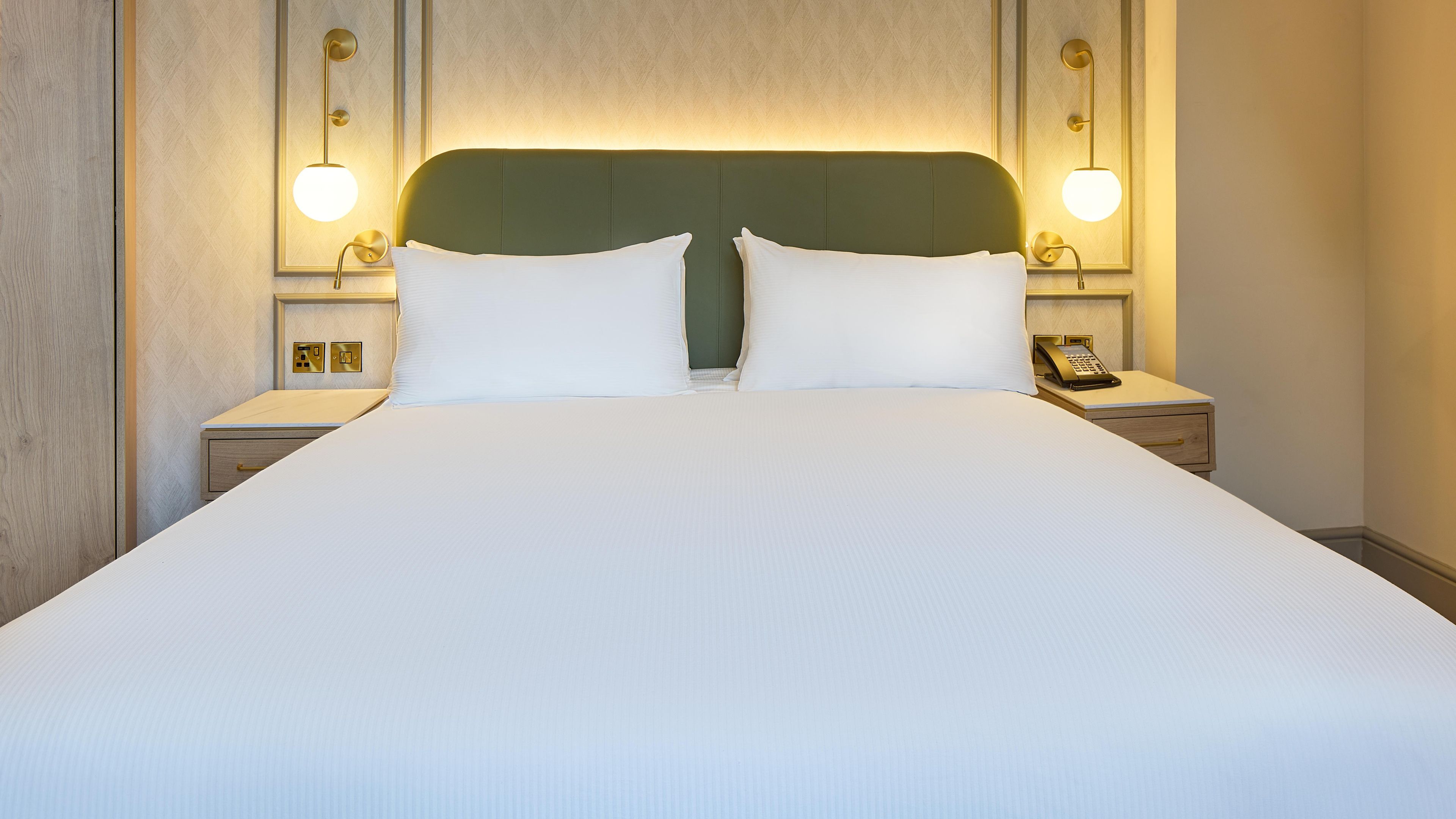 Habitació d'hotel amb un llit gran, dues taules de nit, un telèfon sobre una taula i làmpades subjectes a la paret.