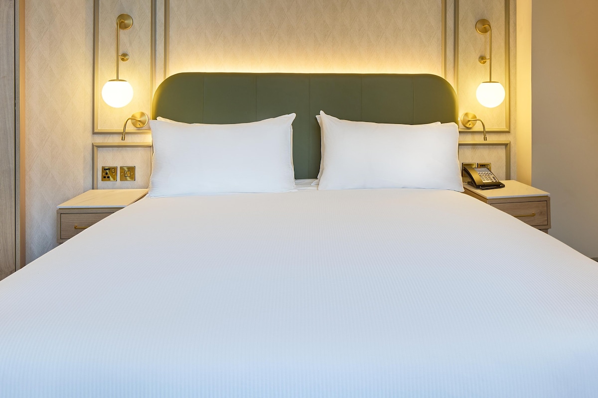 A hotel room with a large bed, two bedside tables, a phone on one table, and wall-mounted lamps.