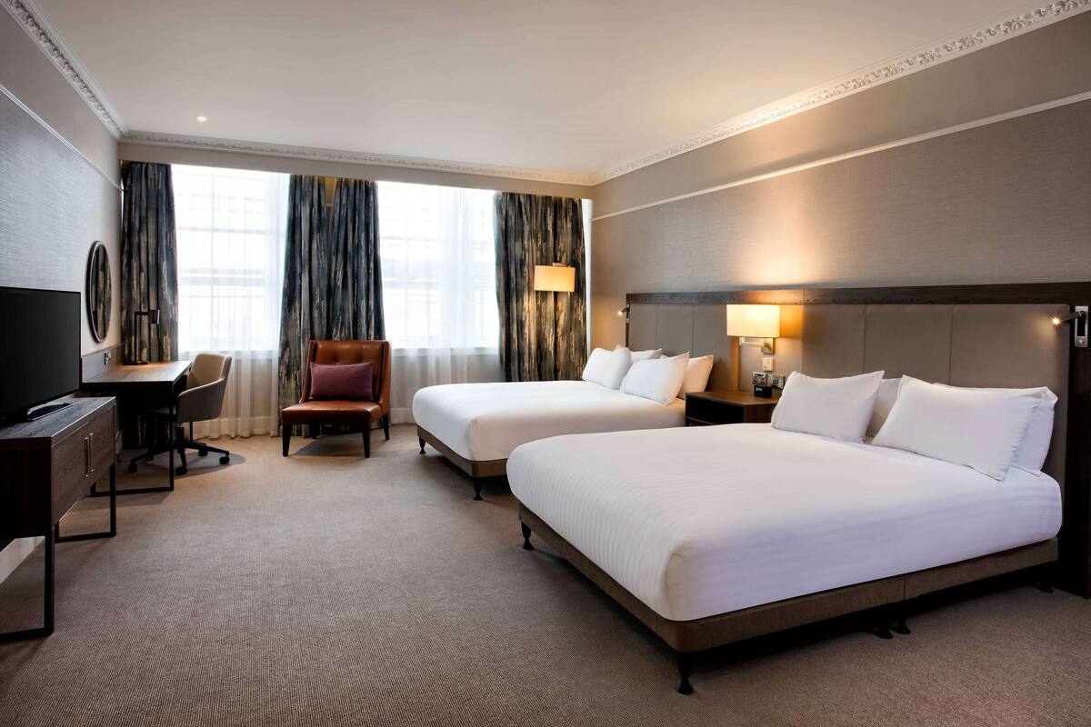 A hotel room with two beds, a desk, a chair, and a television.