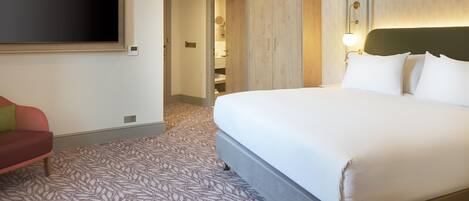 A hotel room with a large bed, a TV mounted on the wall, a wardrobe, and a patterned carpet.