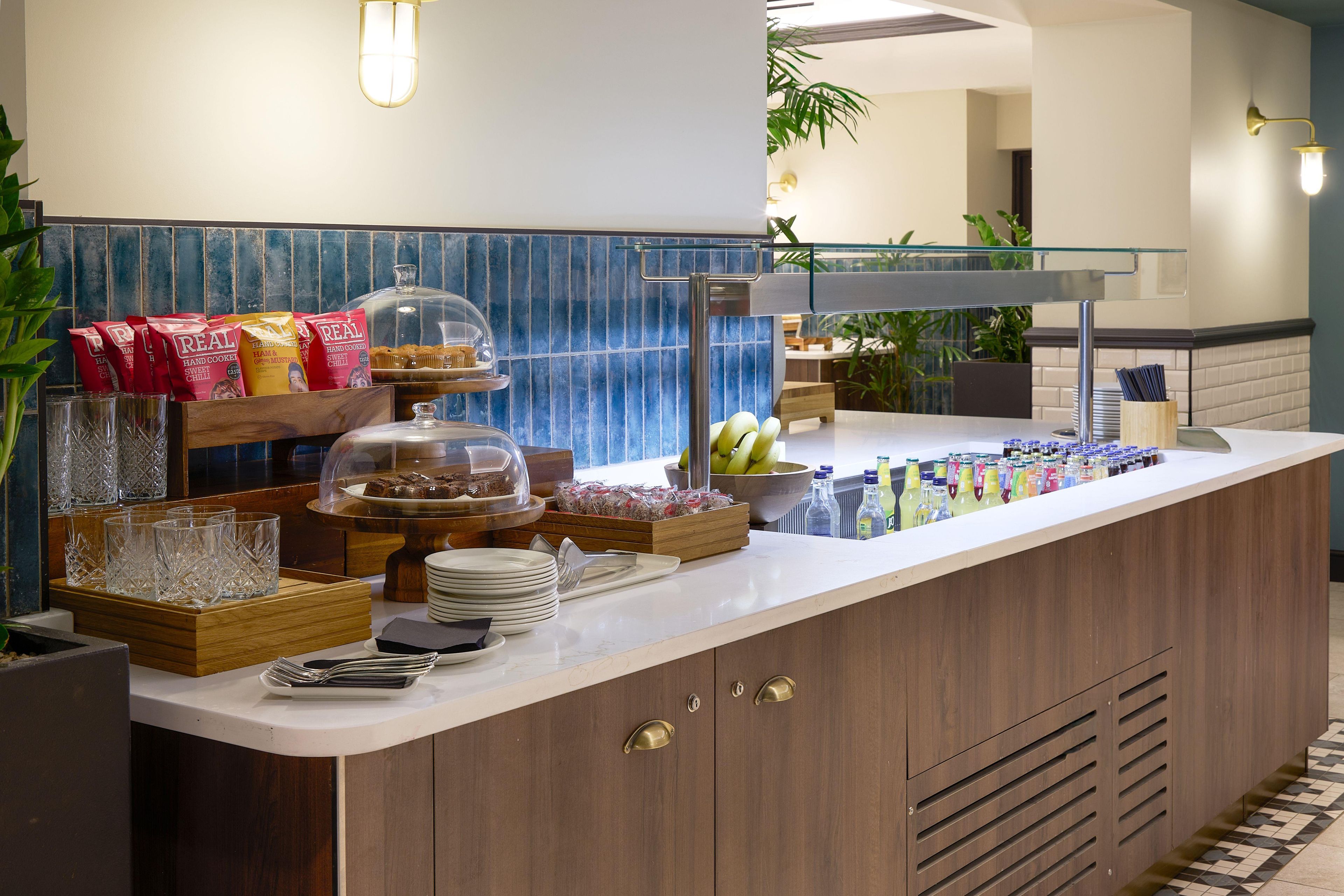 A buffet counter with various food items, glassware, and a fruit bowl.
