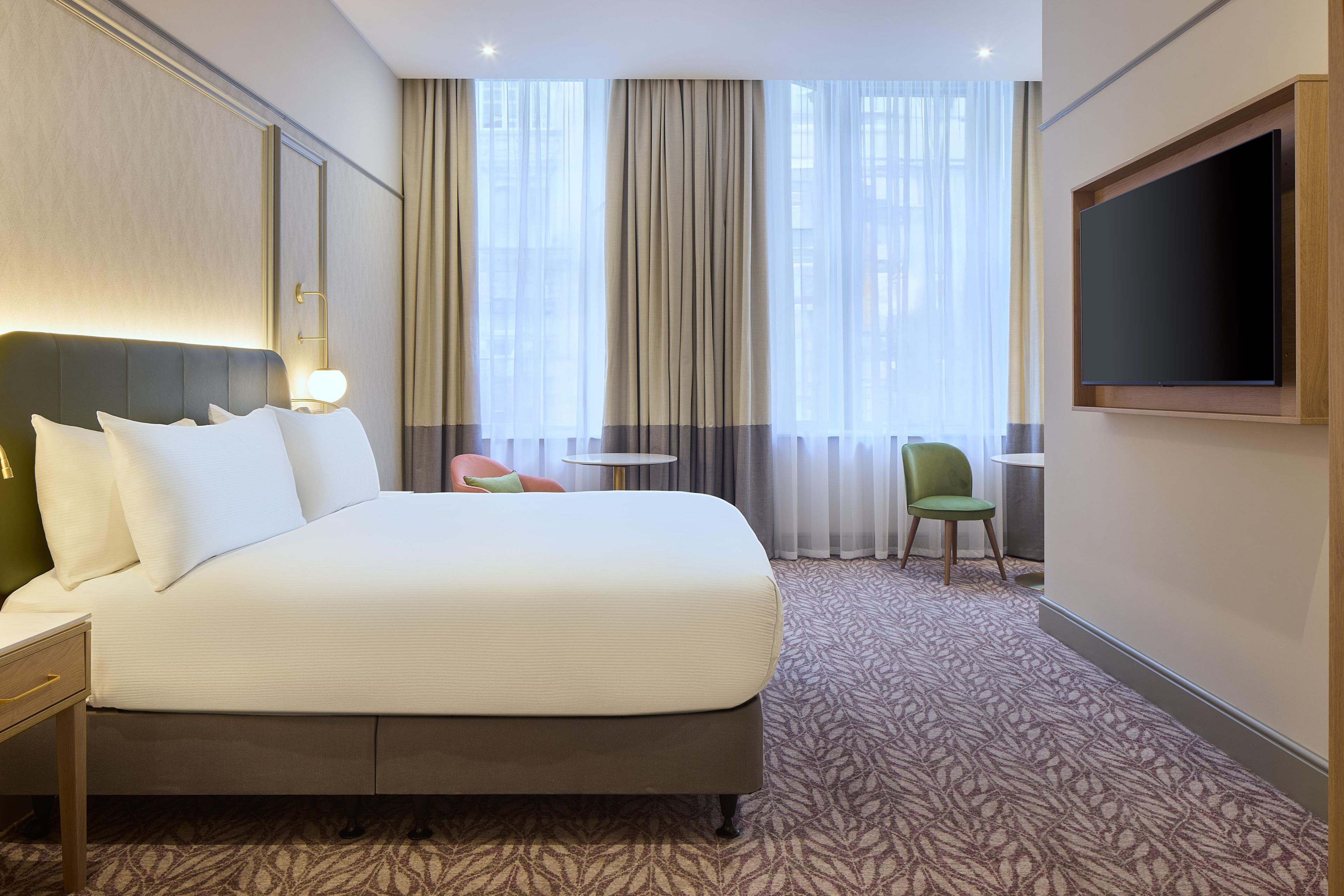 A hotel room with a large bed, a TV, a small table, and a chair.