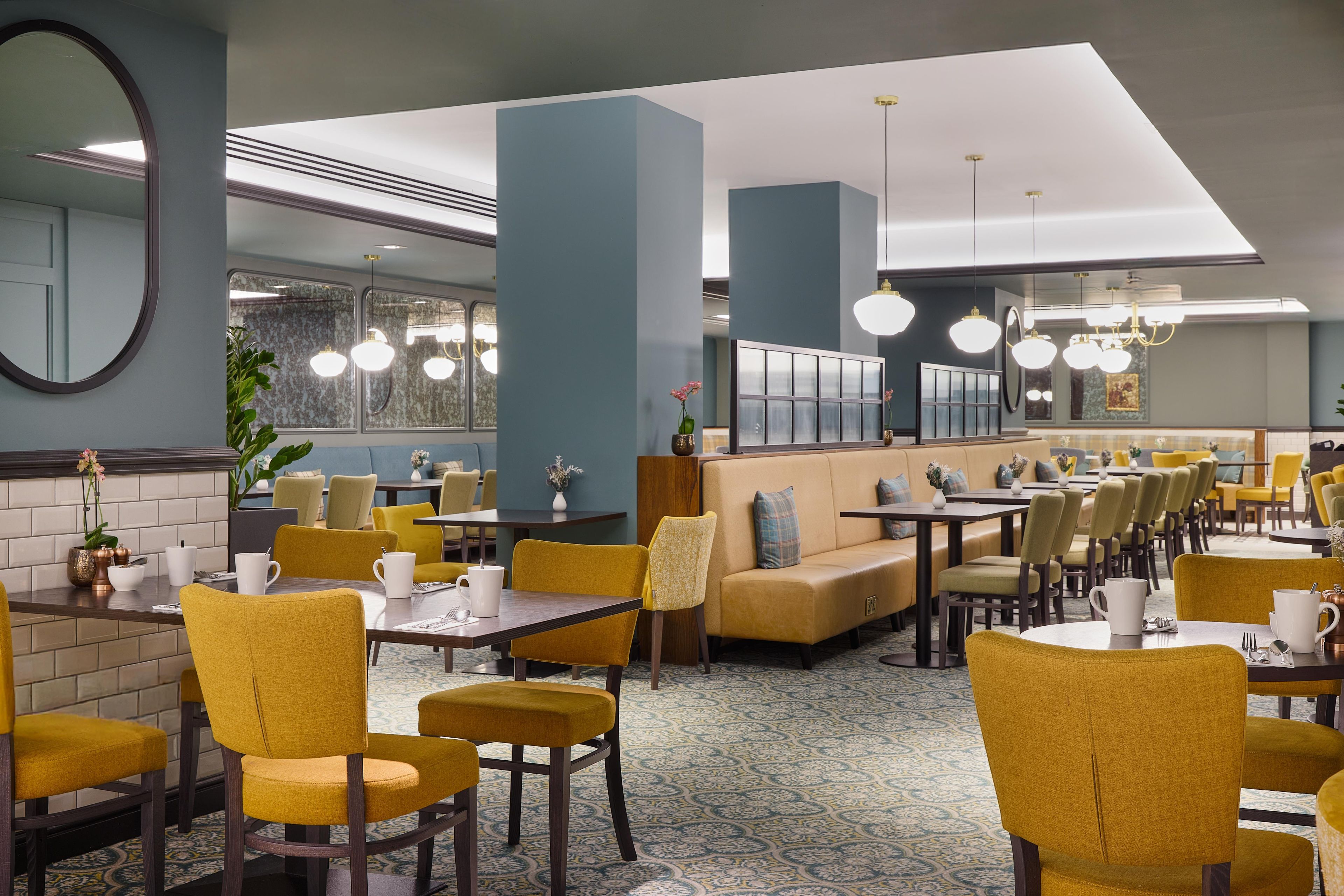 A restaurant with yellow chairs, tables, and a blue wall.