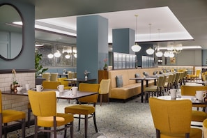 A restaurant with yellow chairs, tables, and a blue wall. - Hilton Edinburgh Carlton (Edinburgh)
