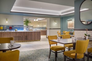 A modern hotel lobby with a central bar area, yellow chairs, and a patterned floor. - Hilton Edinburgh Carlton (Edinburgh)
