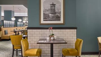 A dining area with a table set for two, a framed cityscape artwork, and a brick wall.