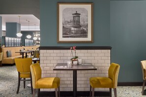 A dining area with a table set for two, a framed cityscape artwork, and a brick wall. - Hilton Edinburgh Carlton (Edinburgh)