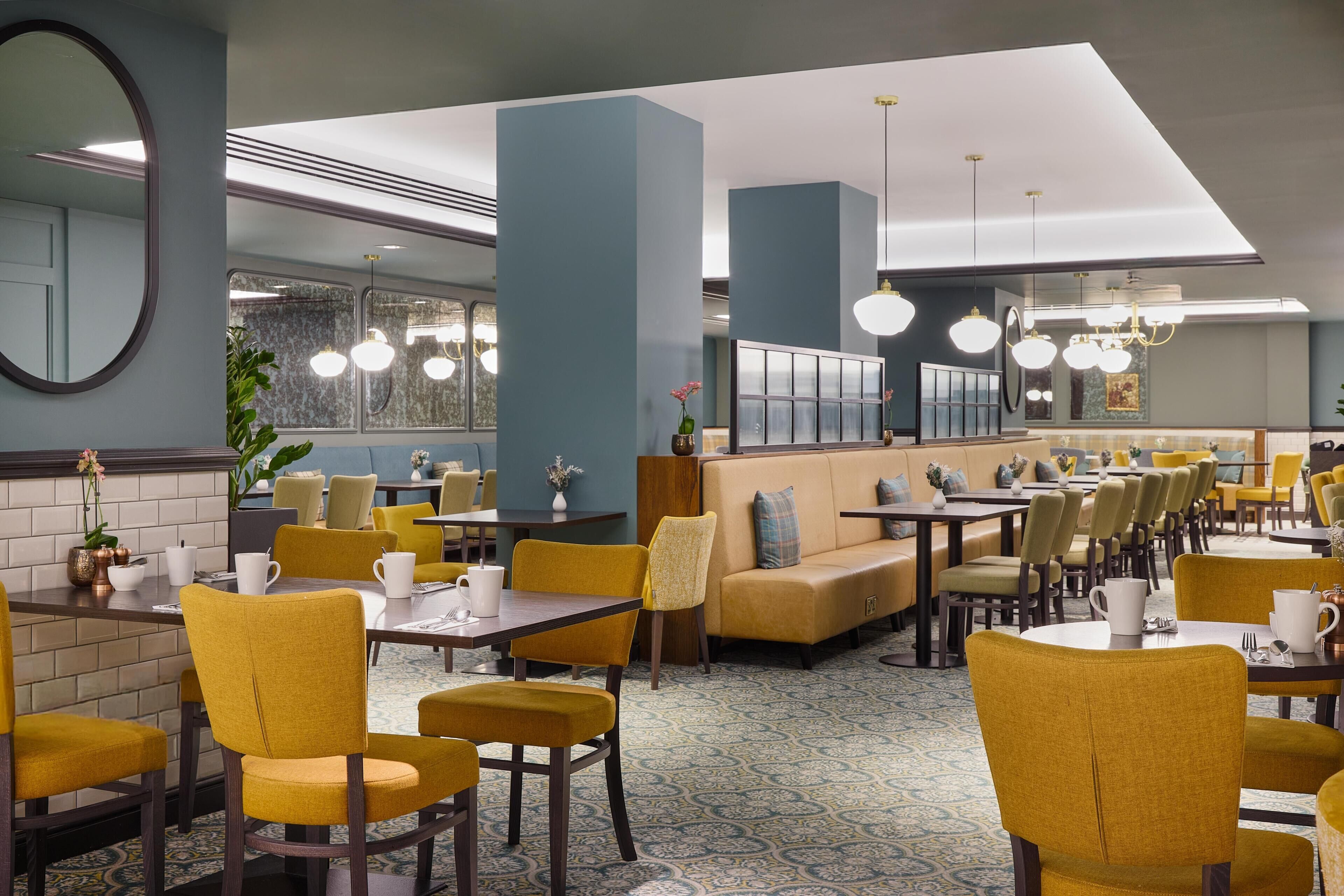 A restaurant with yellow chairs, tables, and a blue wall.