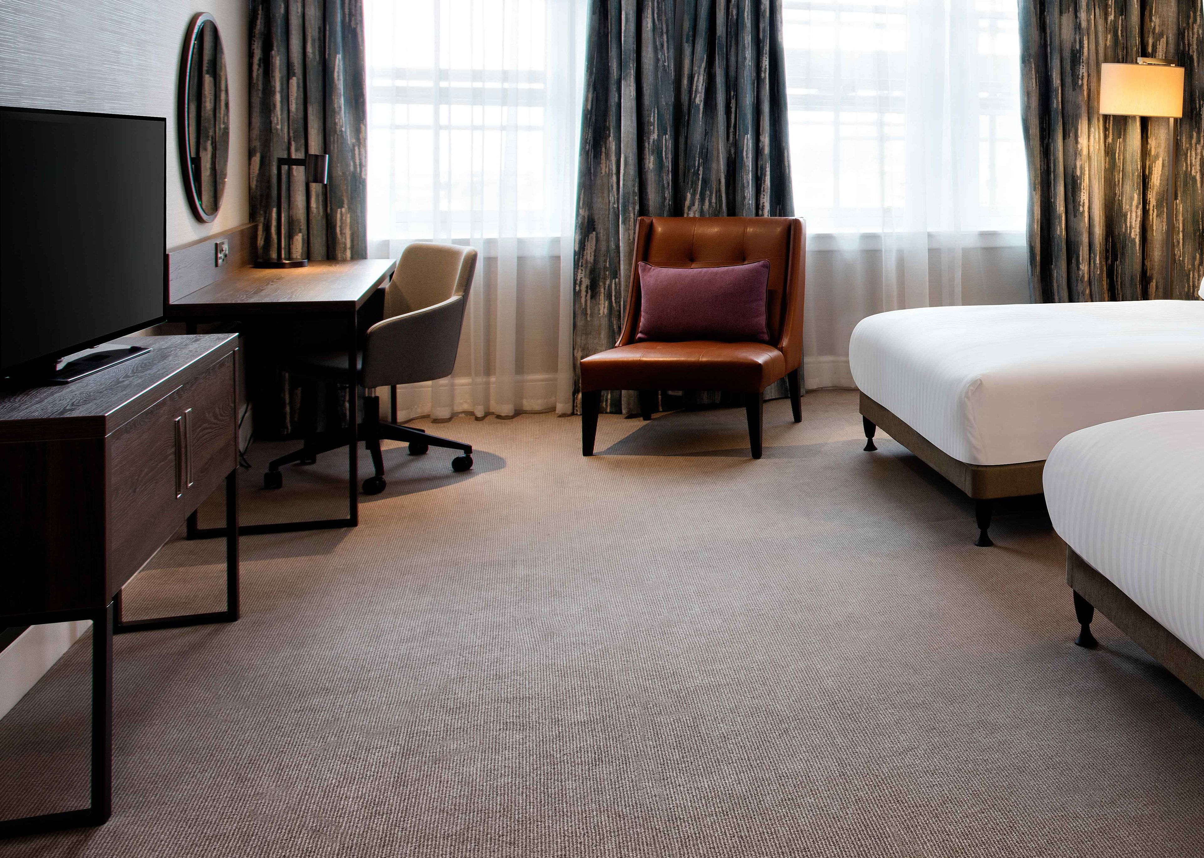 A hotel room with a bed, a desk, a chair, a television, and a large window with curtains.