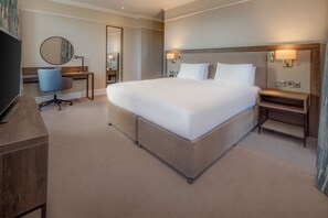 A hotel room with a large bed, a desk with a chair, a TV, and a mirror.