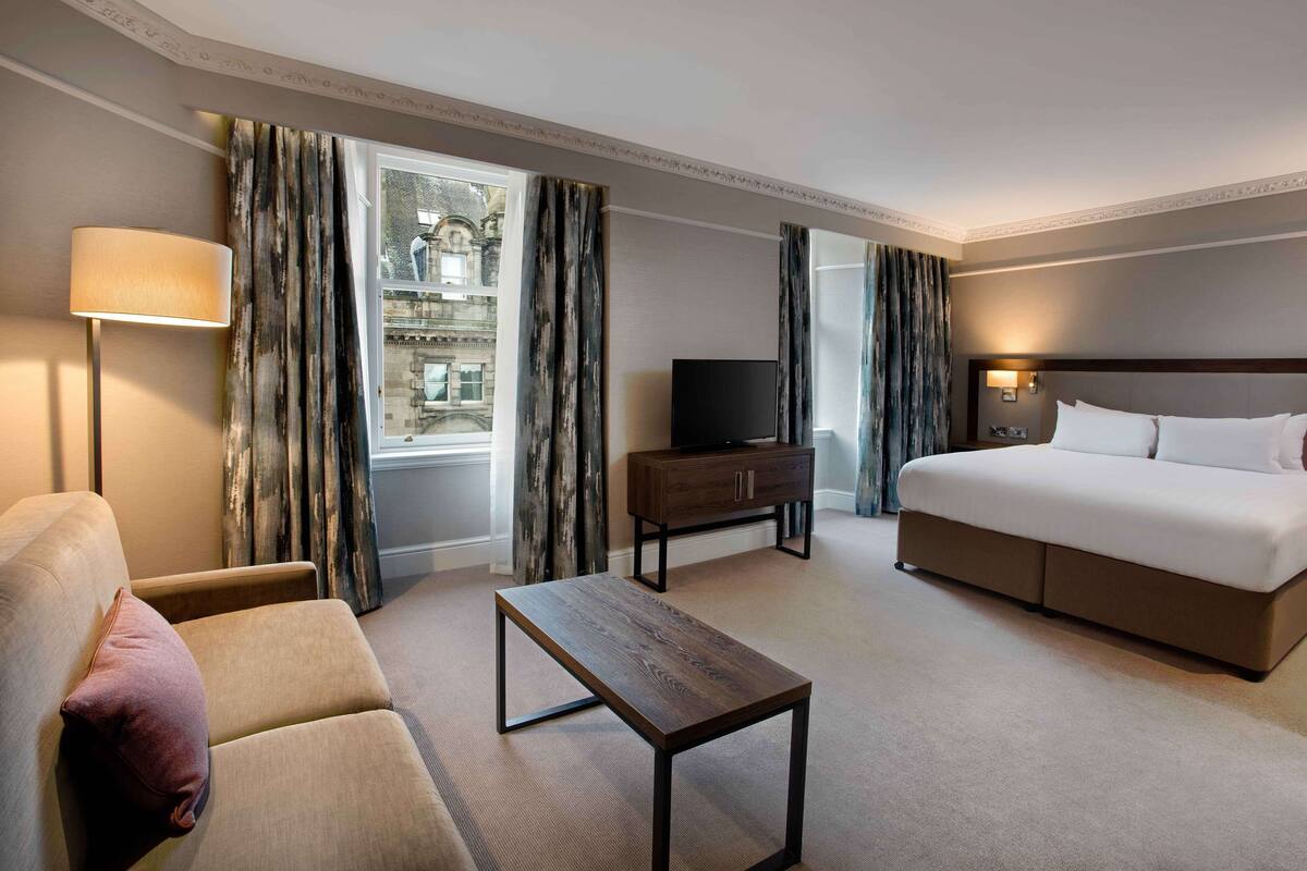 A hotel room with a bed, sofa, TV, and a small table.