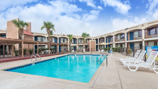 A hotel pool area with a clear blue pool, lounge chairs, and a covered seating area. - Days Inn by Wyndham San Antonio Splashtown/ATT Center (San Antonio)