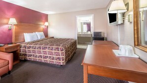 A hotel room with a bed, bedside table, lamp, and a desk with a chair. - Days Inn by Wyndham San Antonio Splashtown/ATT Center (San Antonio)