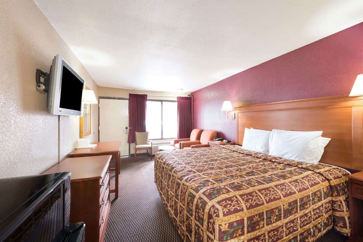 Una habitación de hotel con una cama, un escritorio, un televisor y una ventana con cortinas.