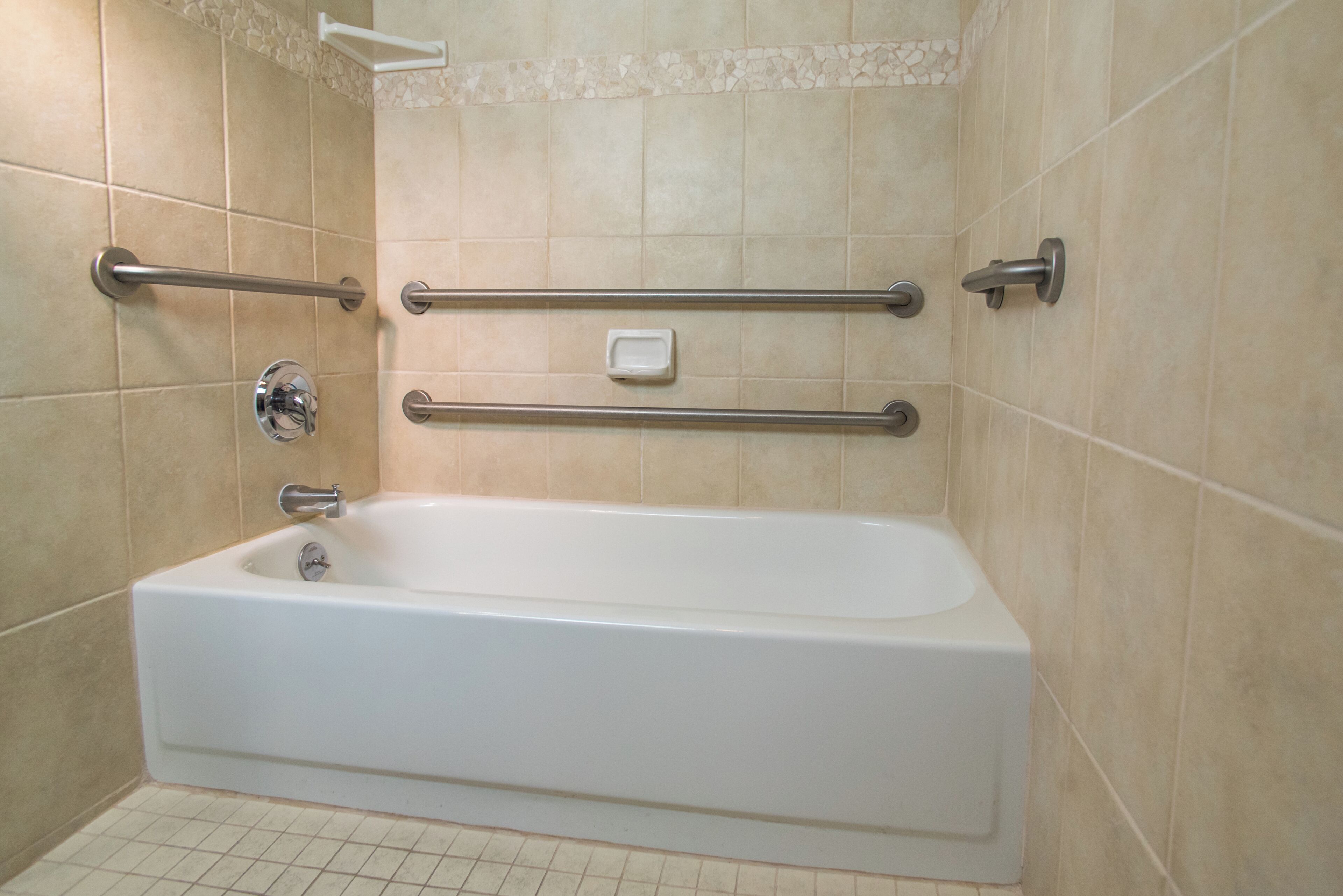 A white bathtub with grab bars, a soap dish, and a tiled shower area.