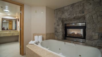 A bathroom with a stone wall, a fireplace, a large bathtub, and a wooden door.