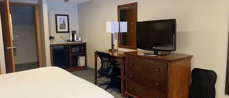 A hotel room with a bed, a desk with a computer, a television, and a dresser.