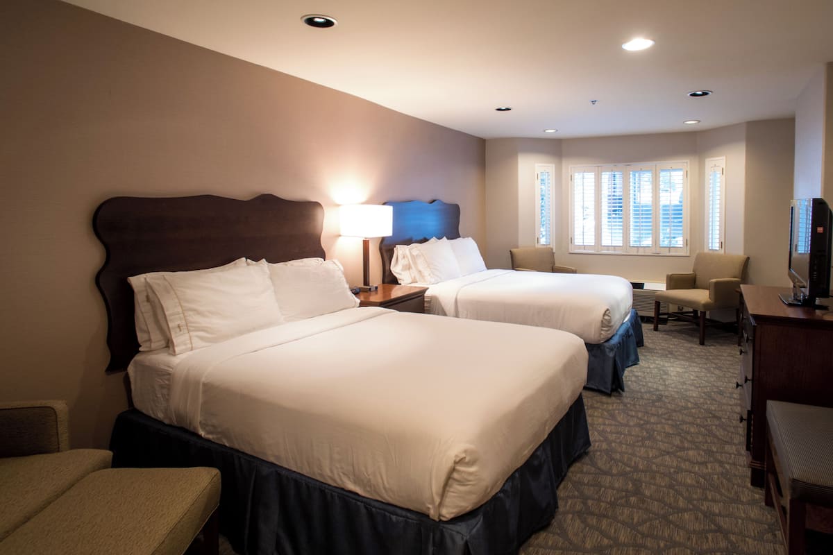 A hotel room with two beds, a desk, a chair, and a television.