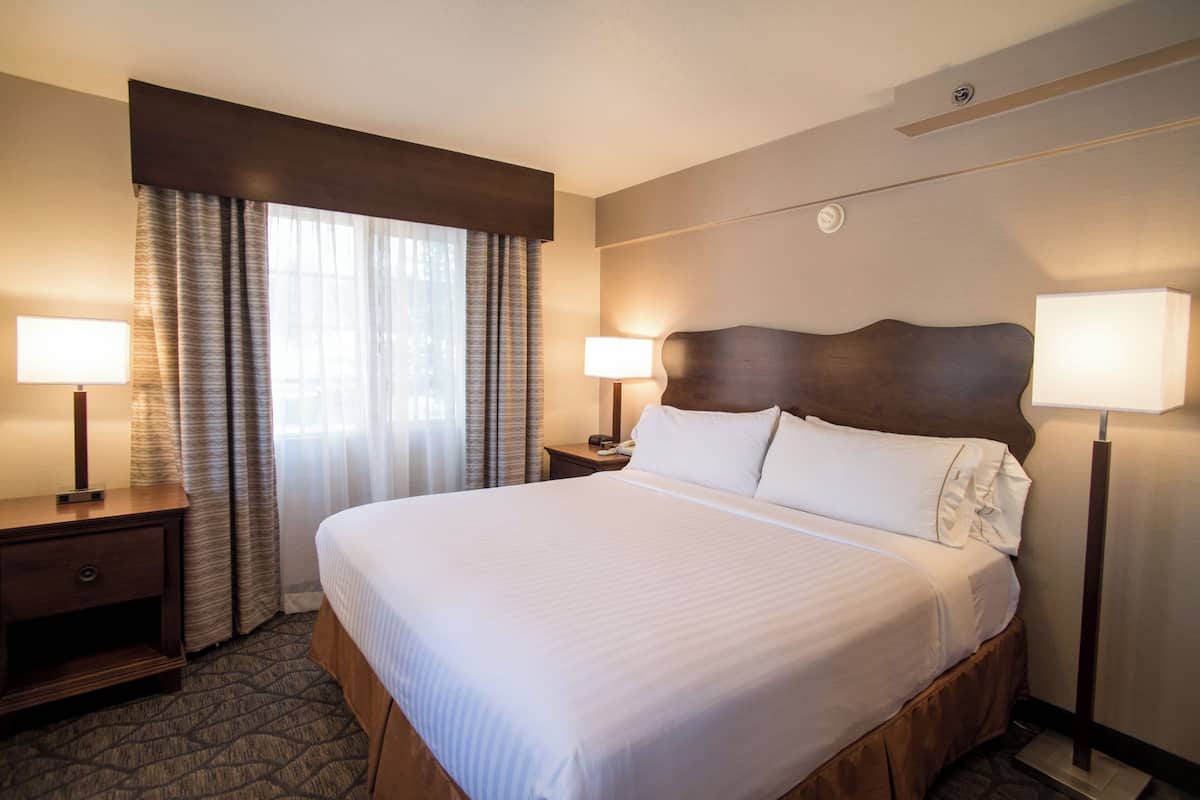 A hotel room with a large bed, two bedside tables, a nightstand, a window with curtains, and two wall-mounted lamps.