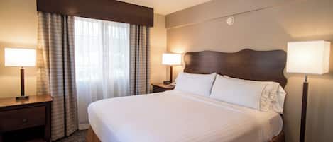 Una habitación de hotel con una cama grande, dos mesitas de noche, una ventana con cortinas y dos lámparas de pared.