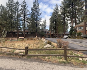 A parking lot with a wooden fence, a bench, and a building with multiple windows and a sloped roof.